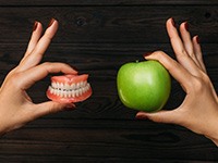 Hands holding a pair of dentures and an apple on wood background