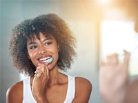 Woman smiling and brushing her teeth in the mirror