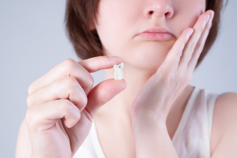 A woman holding a wisdom tooth while suffering mouth pain