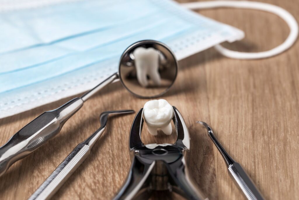 Extracted tooth held by forceps reflected in dental mirror on wooden surface